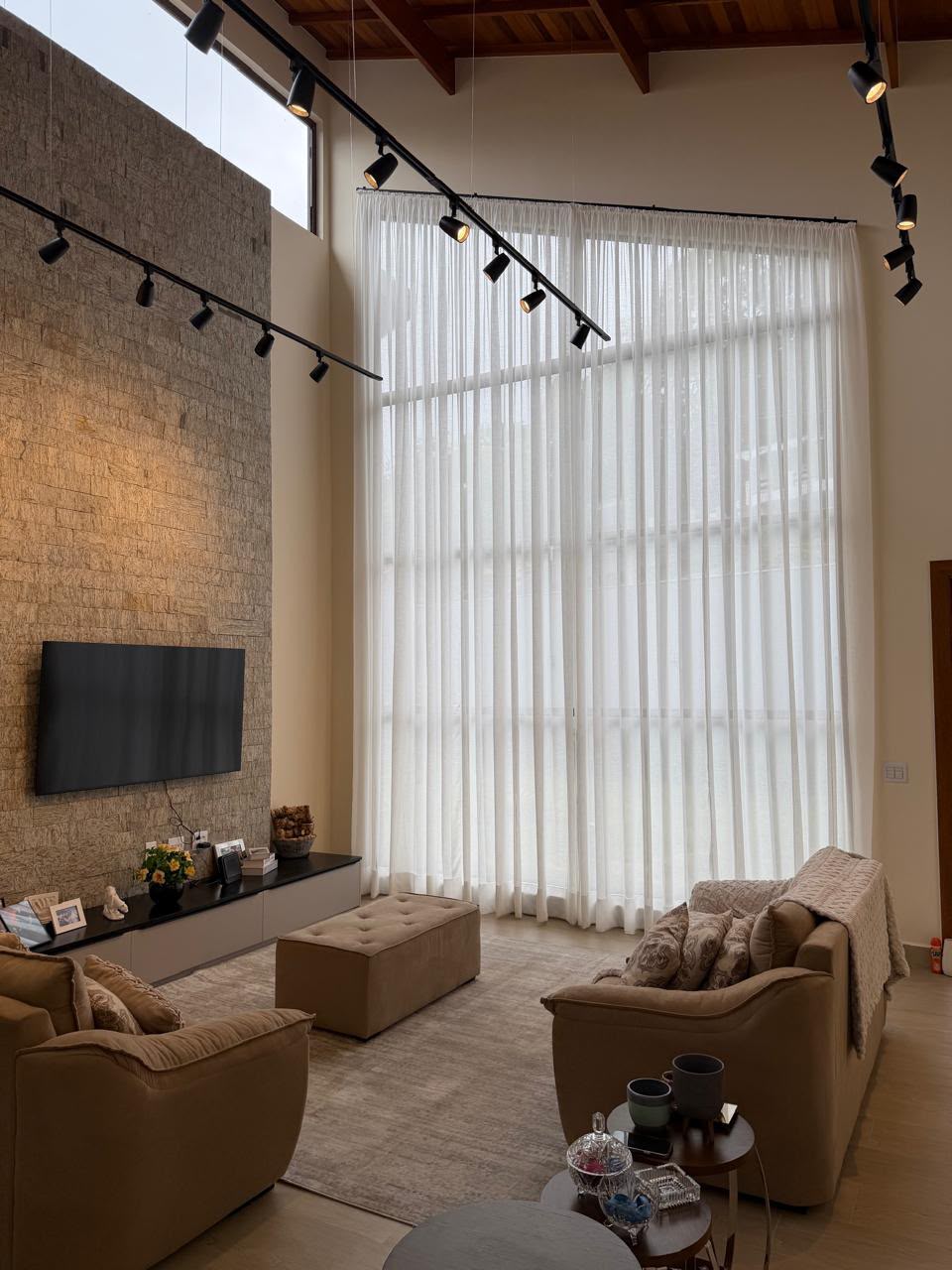 Sala de estar com pé-direito duplo e cortinas de voil instaladas pela Vagner Decor